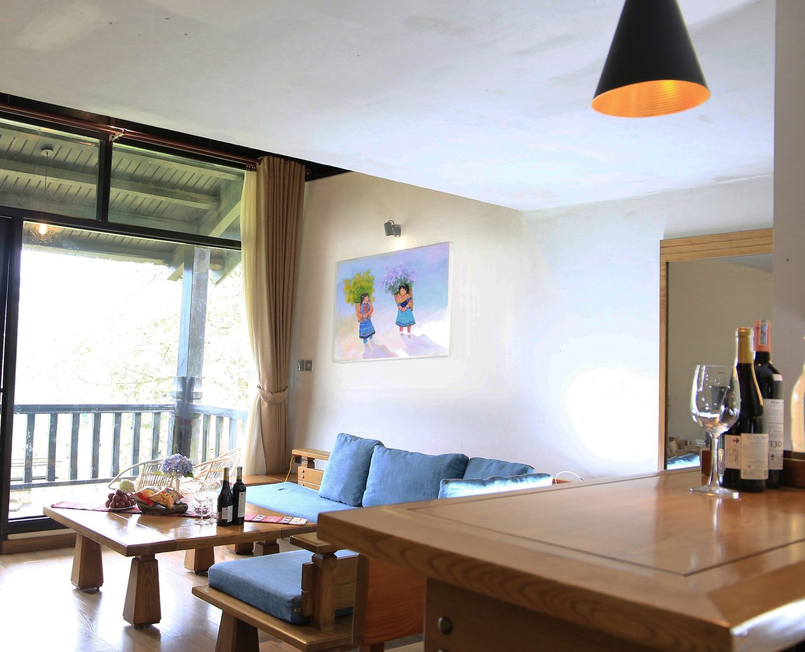 Phòng khách villa đá Heaven House Sapa có lò sưởi đá ốp tường, sofa vải xanh và cửa kính nhìn ra thung lũng